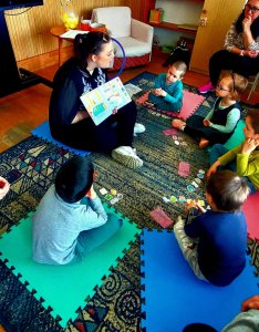 A képen a gyermekek és pedagógusunk egy kis körben ülnek törökülésben és mesejátékot játszanak mágnesek segítségével.