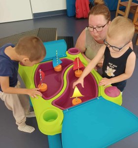 A képen a hajók vízre tétele látható, a gyerekek az általuk készített hajókat tették vízre, és fújják, hogy a hajók ússzanak.