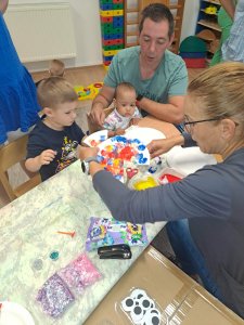 A képen egy asztalnál ülve pedagógusunk közreműködésével folyik a kézműveskedés.