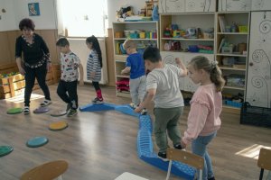 A képen a gyerekek a Tavaszi virág, mozgásfejlesztő játékot használják közösen, egymás után mennek végig az akadálypályán.