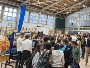 A képen a rendezvényen résztvevők és a kiállítás belső helyszíne látható.