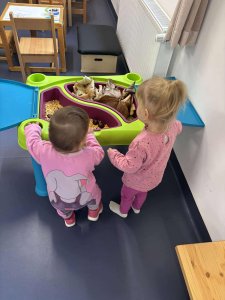 A képen két gyermek látható akik egy asztal mellett állva nézegetik a kihelyezett őszi terméseket.