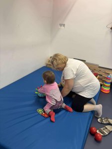 A képen a foglalkozáson résztvevő egyik gyermek és pedagógusunk látható, a torna szőnyegen játszanak.