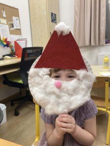 A képen az egyik gyermek látható a Manó műhelyben készített mikulás álarca mögött. 