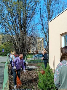 A képen a virágos kertben a kolléganők kerti szerszámokkal tisztítják a talajt.