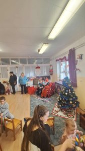 A képen a Mikulás egy fotelben ülve látható amint átadja az ajándékot egy gyermeknek.