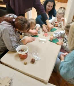 A képen a gyermekek karton karácsonyfákat díszítenek csoportosan egy asztalt körbe ülve.