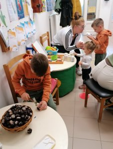 A telephely előterében berendezett foglalkoztatóban egy kisfiú kalapáccsal üti be a fogpiszkálókat a gesztenyébe; így készül a süni. A háttérben testvérei édesanyjukkal foglalatoskodnak kikészített eszközökkel.