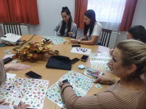 Az asztalnál ülve kipróbálják az óvónők a fejlesztő játékot. A lapokon látható sok kép közül a húzott kártyán levő 3 képet kell megkeresni. A felnőttek számára is élvezetes a saját készítésű játék.