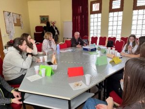 A képen a foglalkozáson résztvevő tanulók és a foglalkozást vezető pedagógusok beszélgetnek egymással egy asztalt körbeülve.