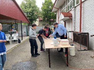 A képen a tanulók egy asztal körül állva hallgatják az előadót, és közben az asztalon meg is tekinthetik előadásának tárgyait.