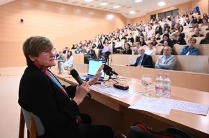 A képen az előadó látható az előadása közben és a vele szemben helyet foglaló hallgatóság. 