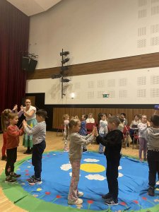 A képen a gyermekek és az előadó végzik közösen a gyakorlatot egy nagy kört rajzolva.