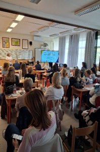 A képen a rendezvényen résztvevők láthatóak egy tanteremben az iskola padokban helyet foglalva, amint figyelemmel kísérik az előadást.