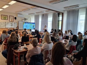 A képen a rendezvényen résztvevők láthatóak egy tanteremben az iskola padokban helyet foglalva, amint figyelemmel kísérik az előadást.