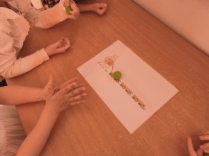 A képen a gyerekek előtt az asztalon egy papír van amin két nyuszi húz három összekötött  kiskocsi, amibe a gyerekek épp zöld korongokat helyeznek.