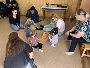 A képen a gyerekek és szüleik egy citerát körbeülve ismerkednek a hangszerrel.
