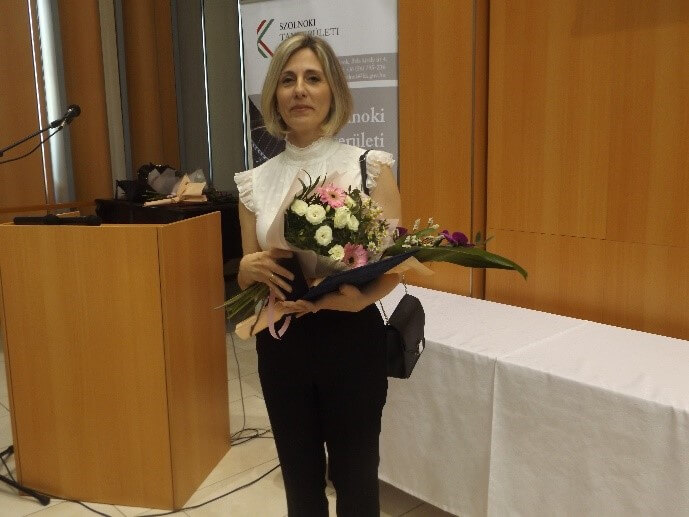 A képen Fejes Nikoletta Pro Talento emlékérmes munkatársunknak látható kezében virággal.