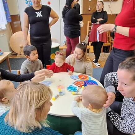 A képen a gyerekek egy asztalt körbeülve, készítik karácsonyfadíszeiket, szüleik és pedagógusaink segítségével.