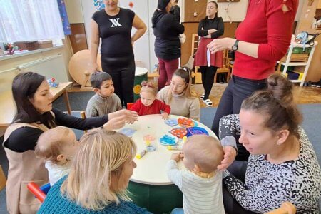 A képen a gyerekek egy asztalt körbeülve, készítik karácsonyfadíszeiket, szüleik és pedagógusaink segítségével.