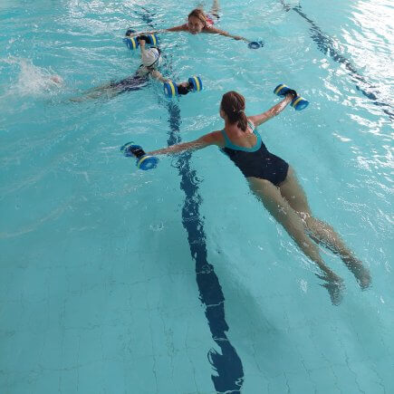 A képen a Szorongás oldása vízben lebegés közben látható. A medencében három személy lebeg a víz tetején kezükben vízi súlyzókkal.