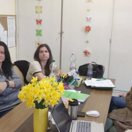 A képen a Jászapáti Tagintézmény szakalkalmazottai egy asztalt körbeülve figyelmesen hallgatják a mesterprogramját bemutató kolléganőt.