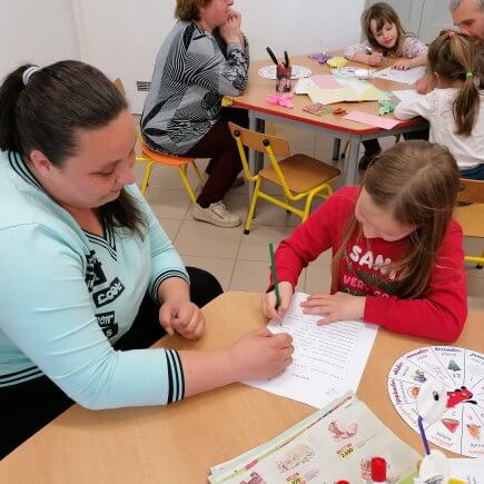 A képen az Újszászi Telephelyen megrendezésre került családi délután pillanata látható, amint a gyerekek szüleikkel közösen töltik a számukra készített fejtörőt.