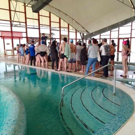 A képen a verseny előtti technikai eligazítás percei láthatóak, amint a medence mellett a versenyzők hallgatják a szervezők által tartott tájékoztatót.