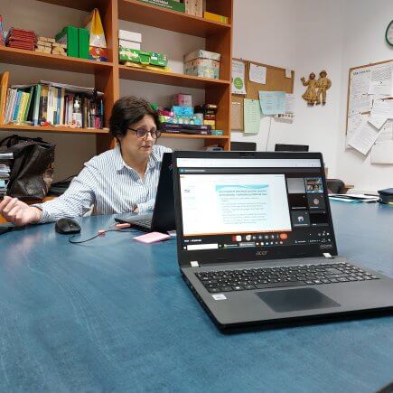 A képen az online műhelyfoglalkozás előadója látható amint egy asztalnál ülve laptopja előtt tartja az előadást, vele szemben egy az online előadáshoz csatlakozott laptop látható amin megjelenik a tartott prezentáció.