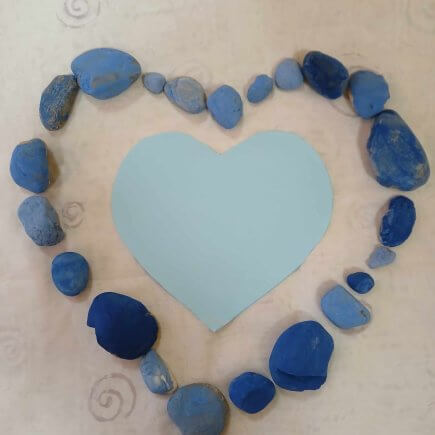 A képen egy kék kövekből kirakott szív alak látható közepén egy kék papírszívvel. A köveket a korai fejlesztésre járó gyermekek festették.