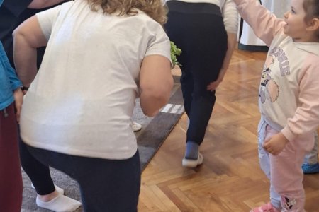 A képen "Bújj, bújj zöld ág" játékot játszanak a szülők és a gyermekek közösen. Az "alagutat" a gyermekek és a szülők közösen alakították ki egy-egy zöld ágacska segítségével, amit a magasba tartottak.