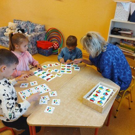 A képen a foglalkozáson részvevő gyermekek egy asztalt körbeülve képességfejlesztő feladatokat végeznek pedagógusunk segítségével.