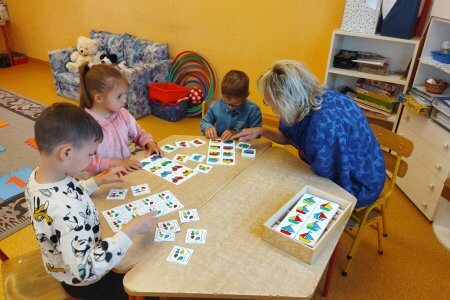 A képen a foglalkozáson részvevő gyermekek egy asztalt körbeülve képességfejlesztő feladatokat végeznek pedagógusunk segítségével.