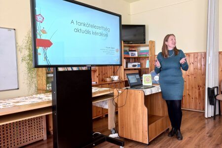 A képen a fórum előadója látható az interaktív tábla mellett állva tartja az előadását.