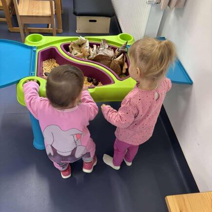 A képen két gyermek látható akik egy asztal mellett állva nézegetik a kihelyezett őszi terméseket.