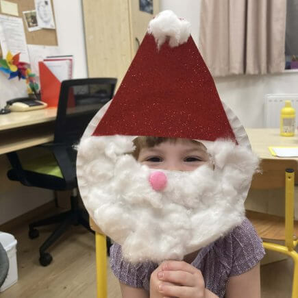 A képen az egyik gyermek látható a Manó műhelyben készített mikulás álarca mögött.