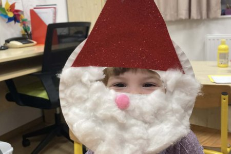 A képen az egyik gyermek látható a Manó műhelyben készített mikulás álarca mögött.