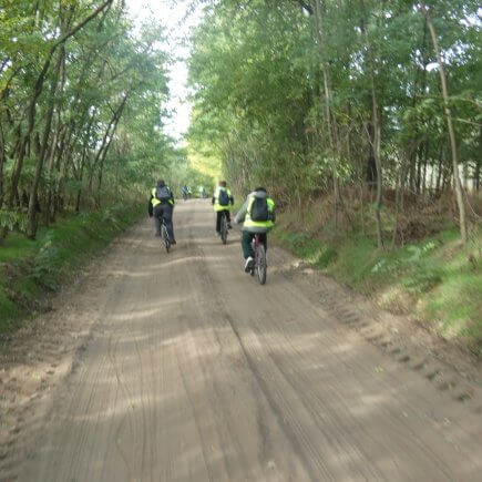 A képen a kerékpártúrán résztevők áthatóak amint egy földúton tekernek a fák között.
