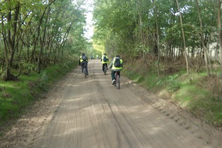 A képen a kerékpártúrán résztevők áthatóak amint egy földúton tekernek a fák között.