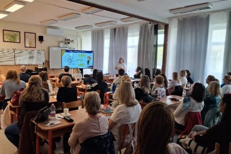 A képen a rendezvényen résztvevők láthatóak egy tanteremben az iskola padokban helyet foglalva, amint figyelemmel kísérik az előadást.
