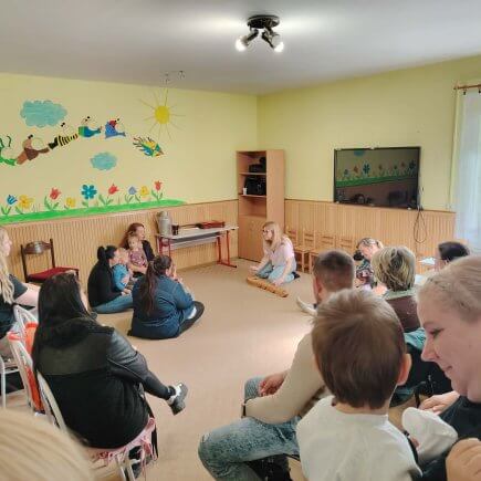 A képen a foglalkozáson résztvevők és az előadó látható, amint a teremben közösen dalolnak citera kíséretében.