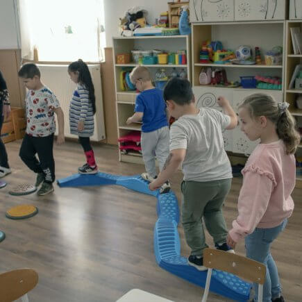 A képen a gyerekek a Tavaszi virág, mozgásfejlesztő játékot használják közösen, egymás után mennek végig az akadálypályán.