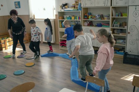 A képen a gyerekek a Tavaszi virág, mozgásfejlesztő játékot használják közösen, egymás után mennek végig az akadálypályán.