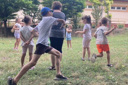 A képen az Elvesztettem zsebkendőmet… népi játék az udvaron látható. A gyerekek körben állnak, és két játékos kergeti egymást.
