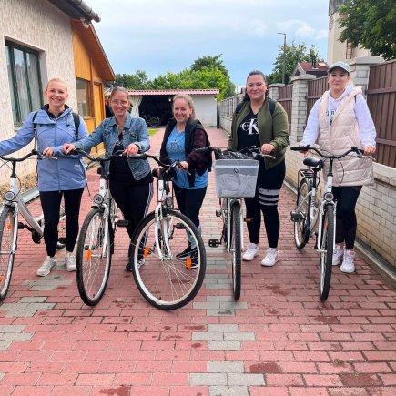 A képen a Kunhegyesi Tagintézmény munkatársai láthatóak a csapatépítő kerékpározás előtt egy kocsibejárón, kerékpárjaik mellett.
