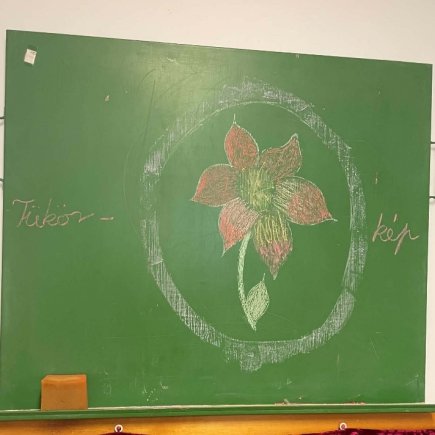 A képen az Önismereti tábor logója látható a zöld iskolai táblára színes krétával felrajzolva, egy fehér körben egy piros virág.